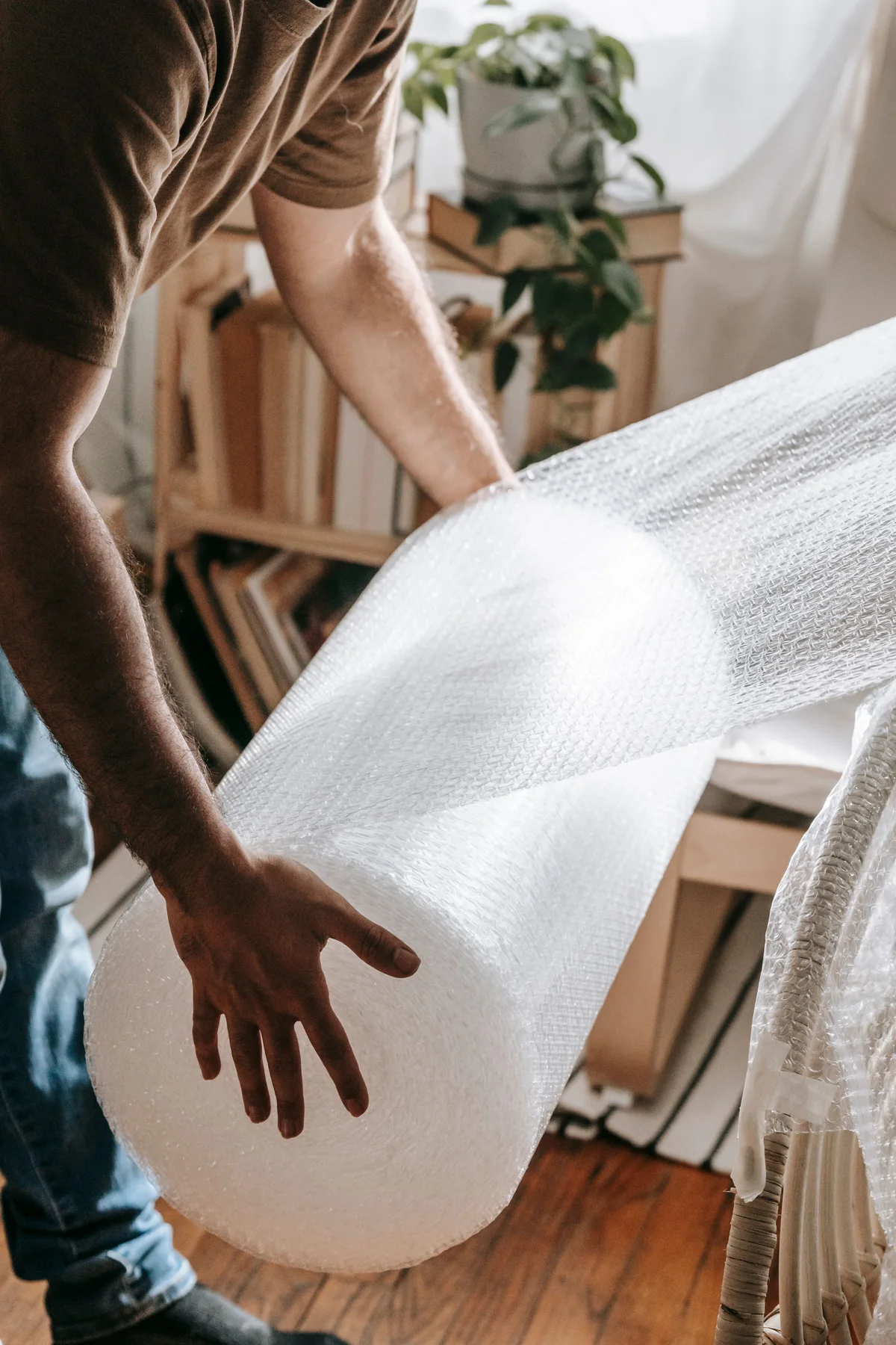 A person holding bubble wrap beside a partially wrapped chair