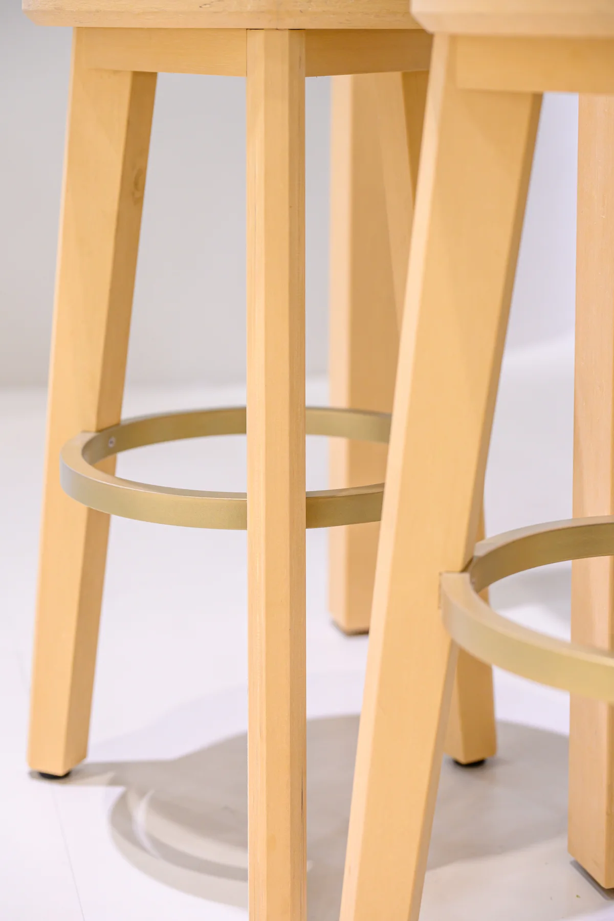 Legs, circular footrails and visible fixings of two pale exhibition stools