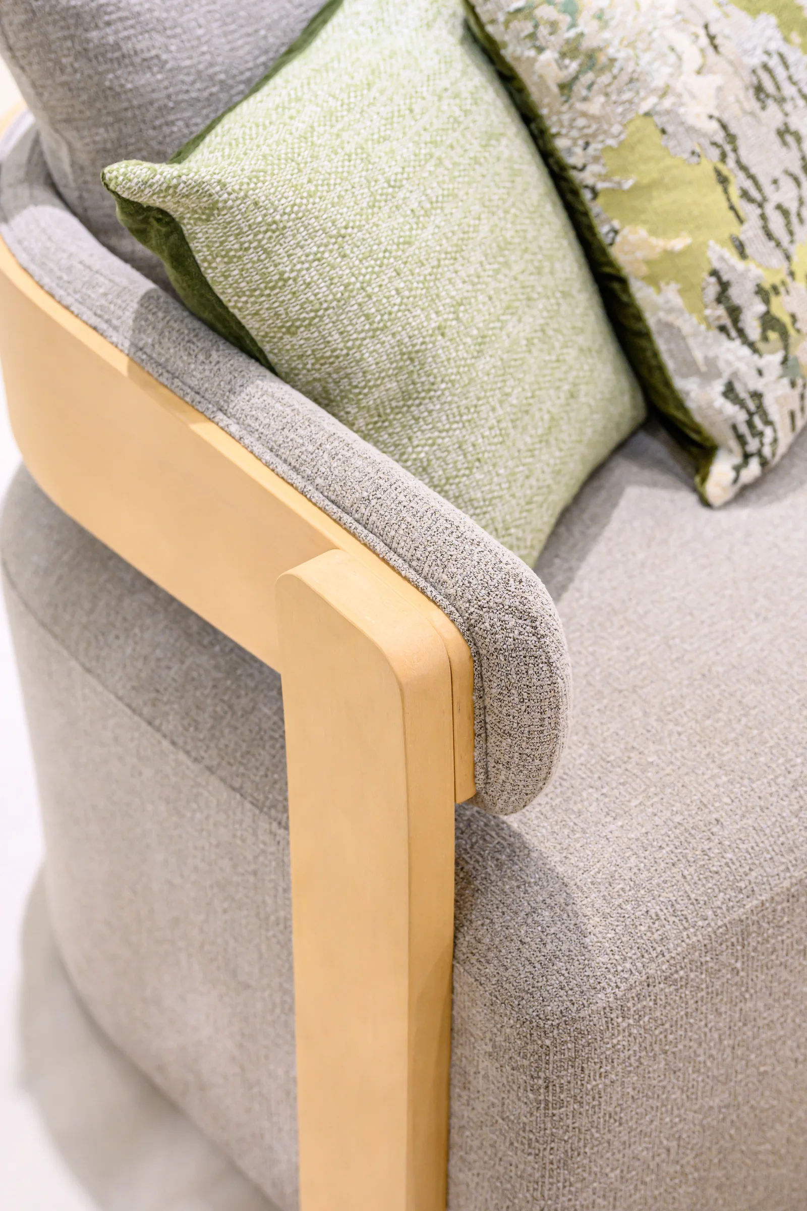 Grey seat cushion with green and patterned pillows inside a warm-toned chair frame