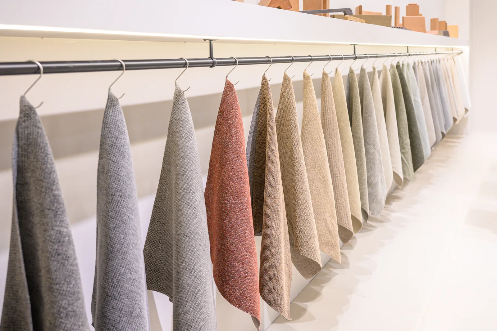 Hanging textile samples in neutral and muted colours on an exhibition rail