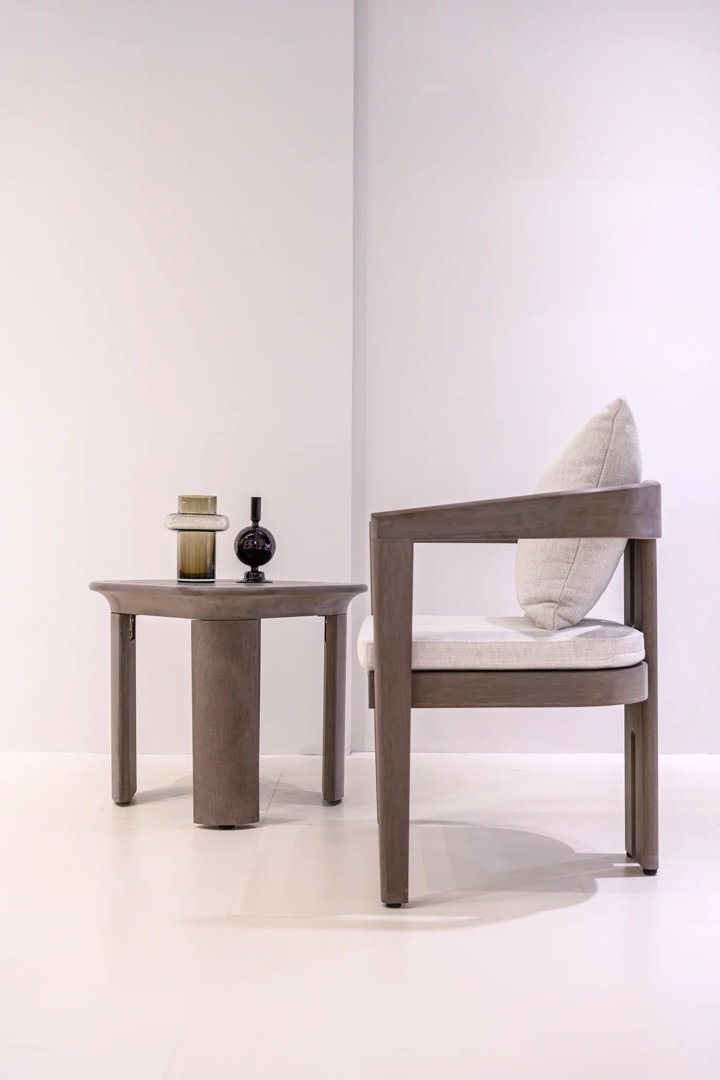 Side view of a grey-brown chair with pale cushions beside a round table