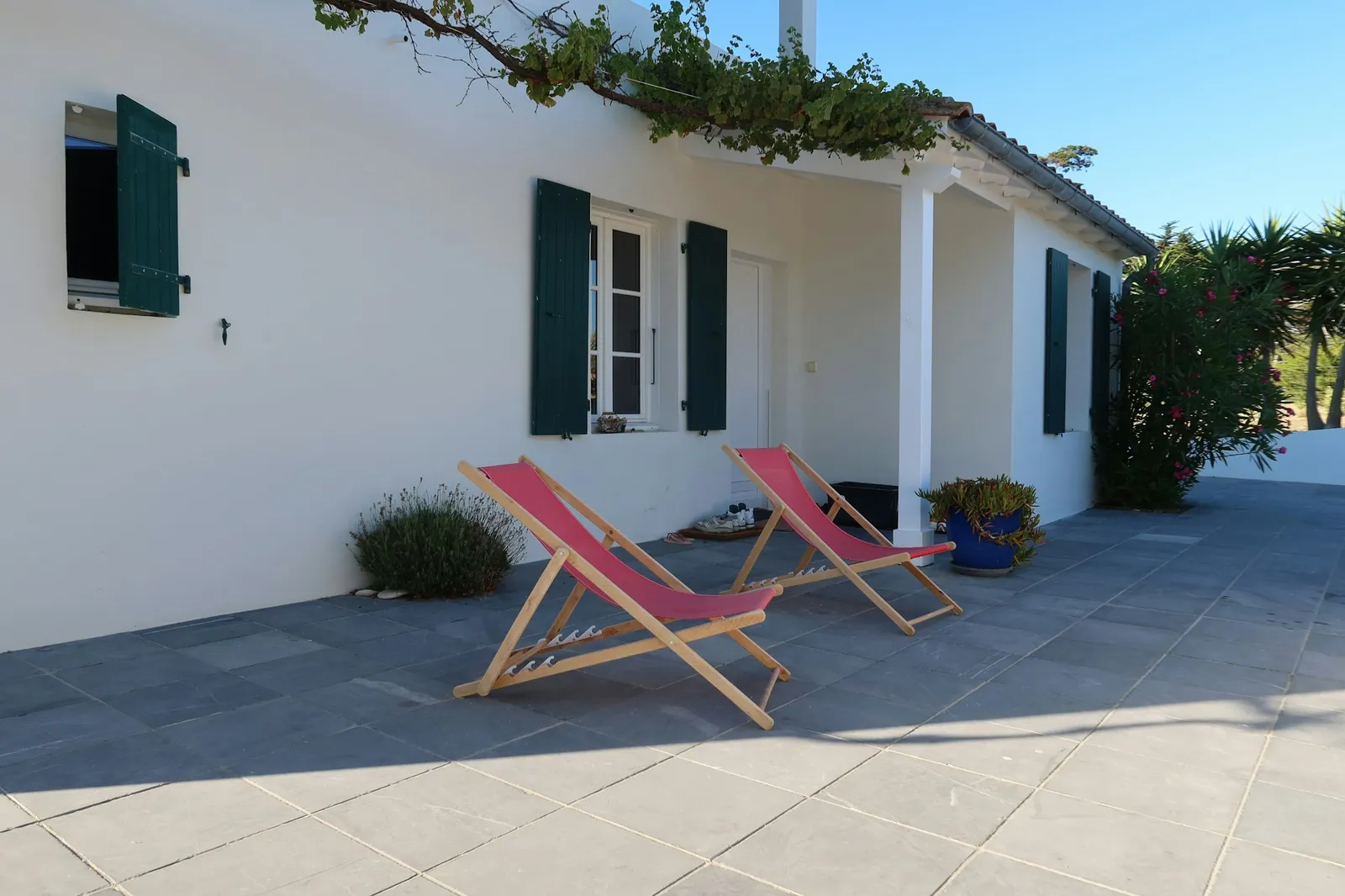 Two red deckchairs on a paved terrace outside a white house