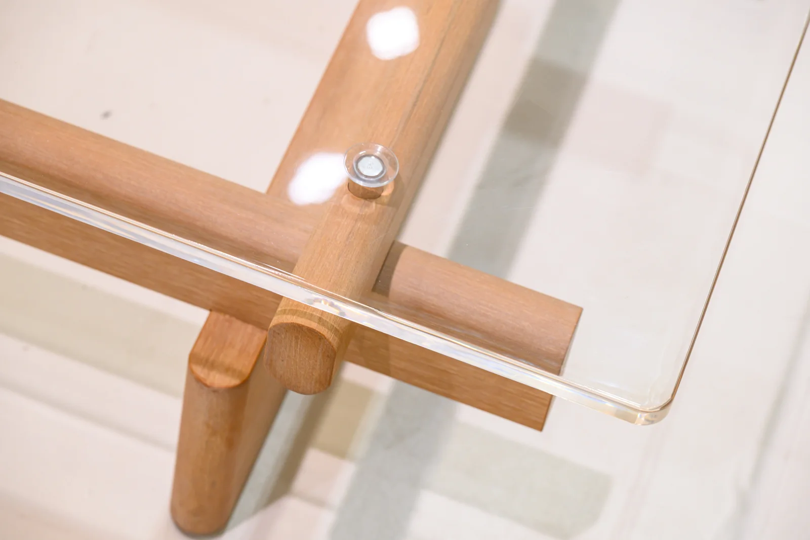 Transparent tabletop corner above crossing frame members and a visible fixing
