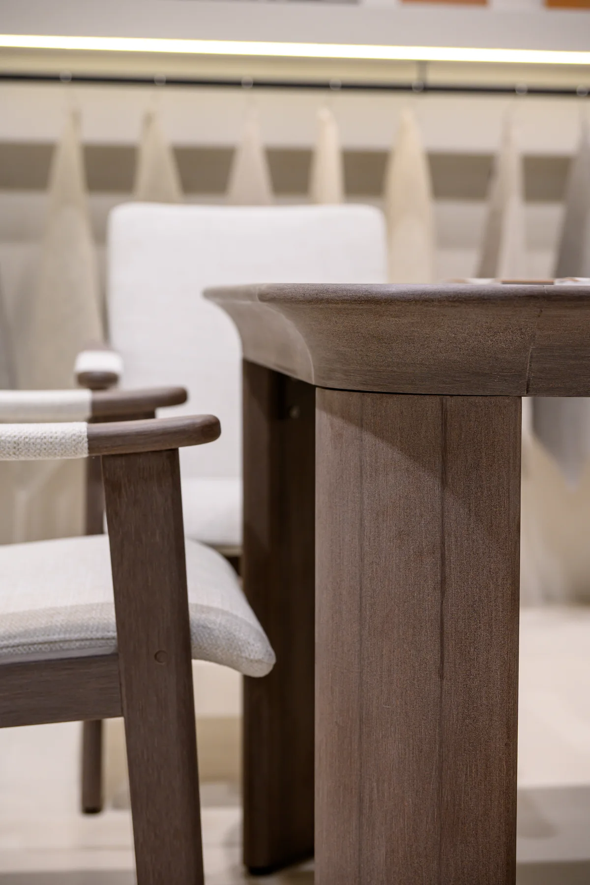 Rounded dark tabletop edge above a broad leg beside upholstered chairs