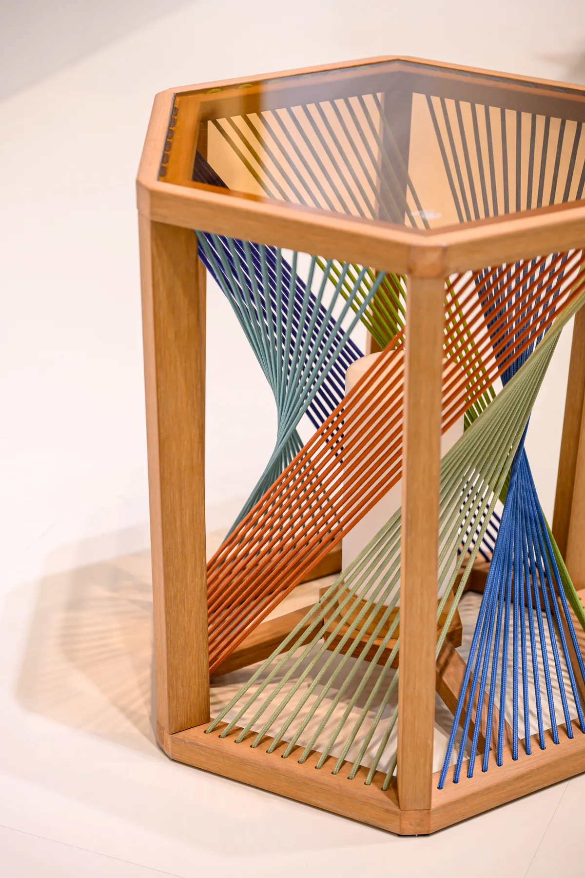 Polygonal table with a transparent top and coloured cords between its frame members